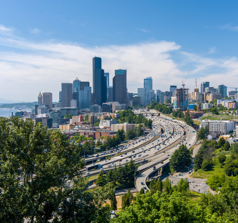 panoramic_seattle_view_corporate_housing Panoramic view of downtown Seattle with highways, modern buildings, and greenery—showcasing the city’s accessibility for corporate housing guests.