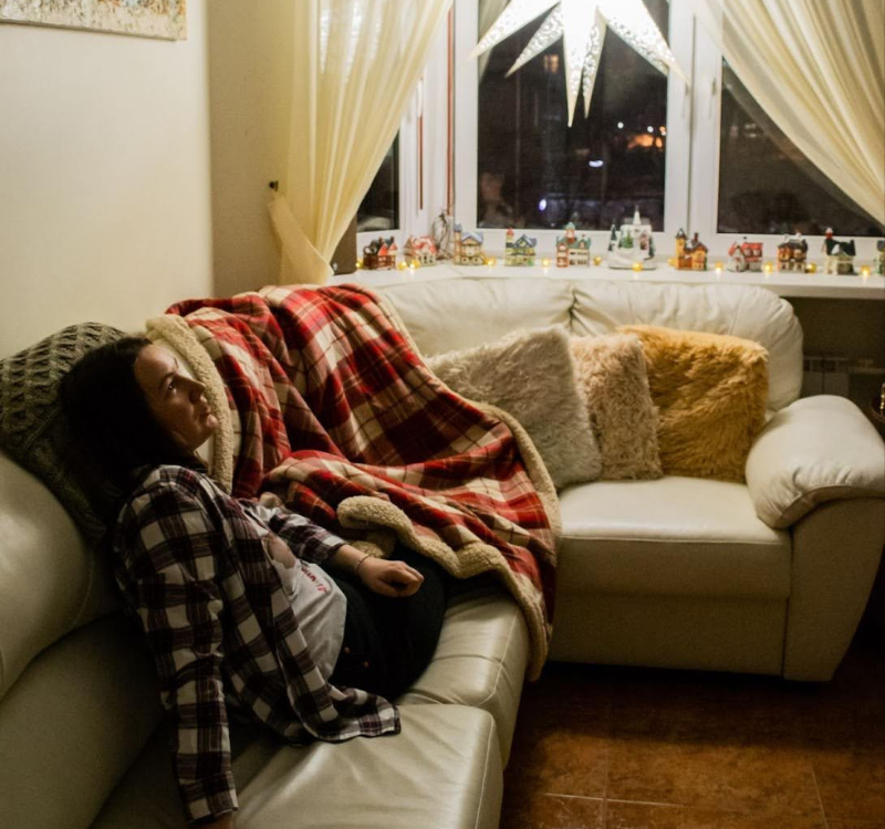 How to Make Your Aplus Housing Temporary Stay Feel Like Home (4) Young woman relaxing on a cozy couch with soft blankets and pillows, capturing how to make your Aplus Housing temporary stay feel like home.