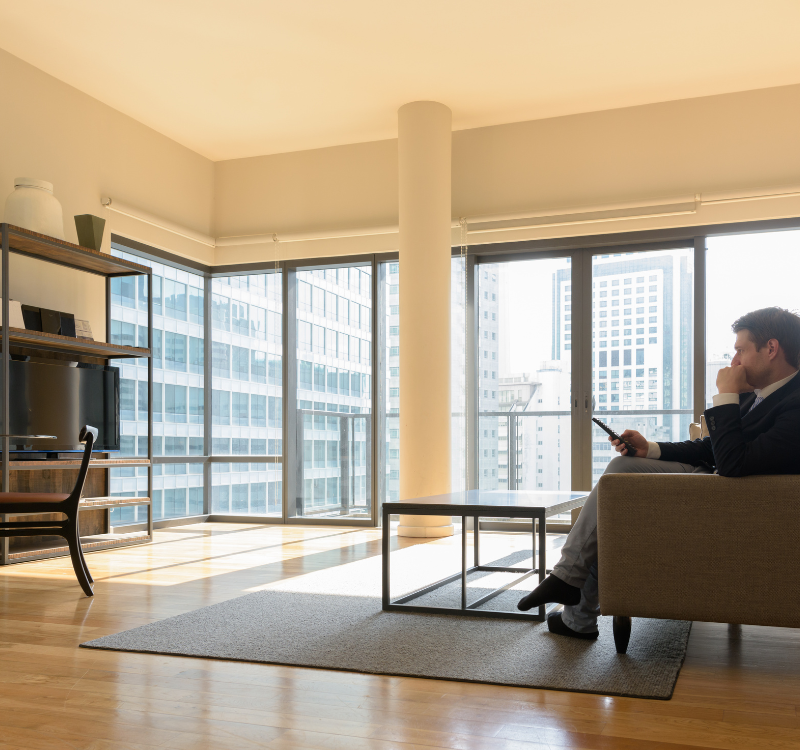 Corporate Business Housing The Ultimate Solution for Professionals on the Go (1) Businessman sitting in a modern furnished apartment with city views, using a smartphone—ideal representation of Corporate Business Housing comfort and style.